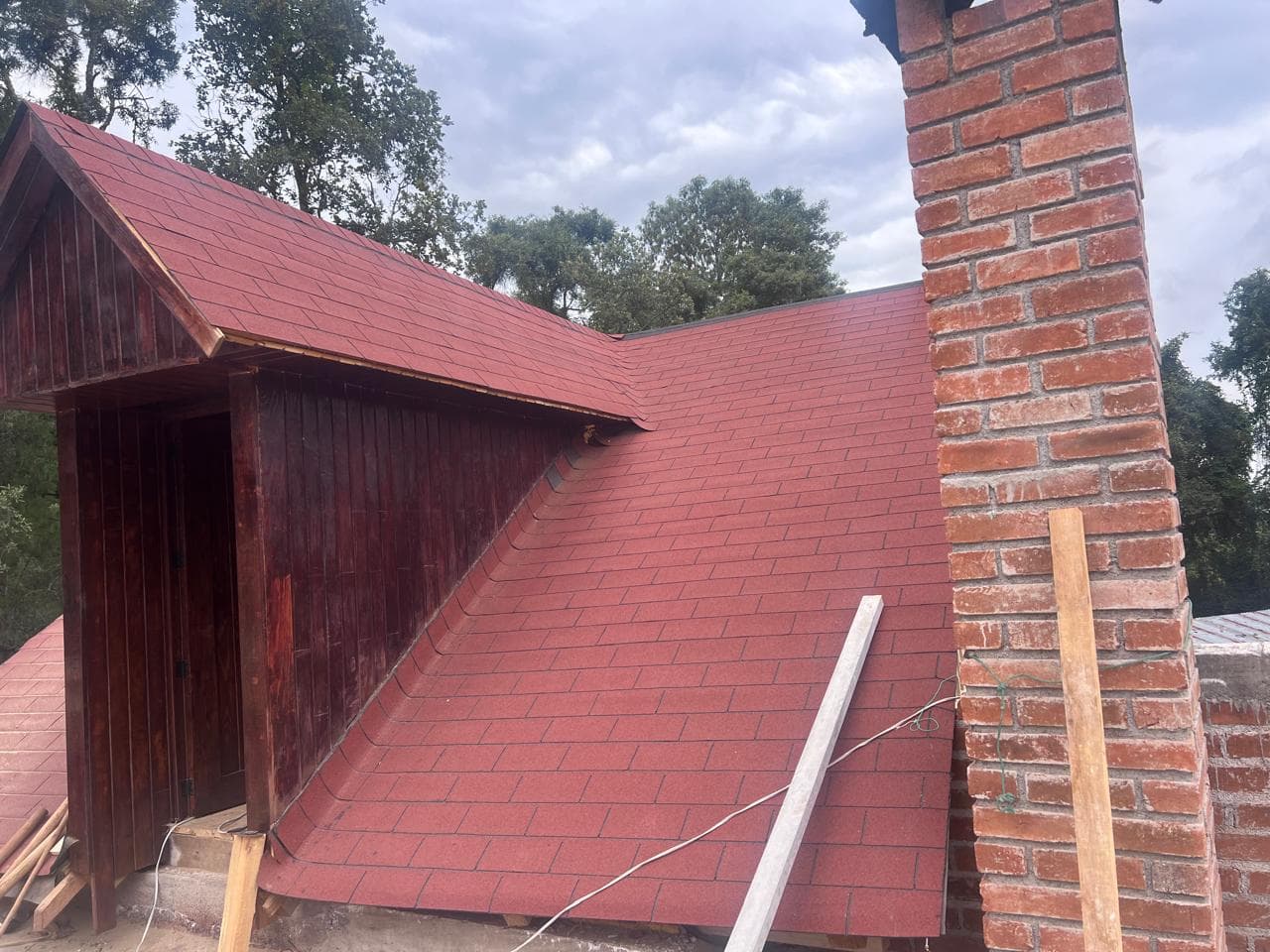Vista exterior de una cubierta inclinada restaurada con teja asfáltica roja junto a una chimenea de ladrillo.