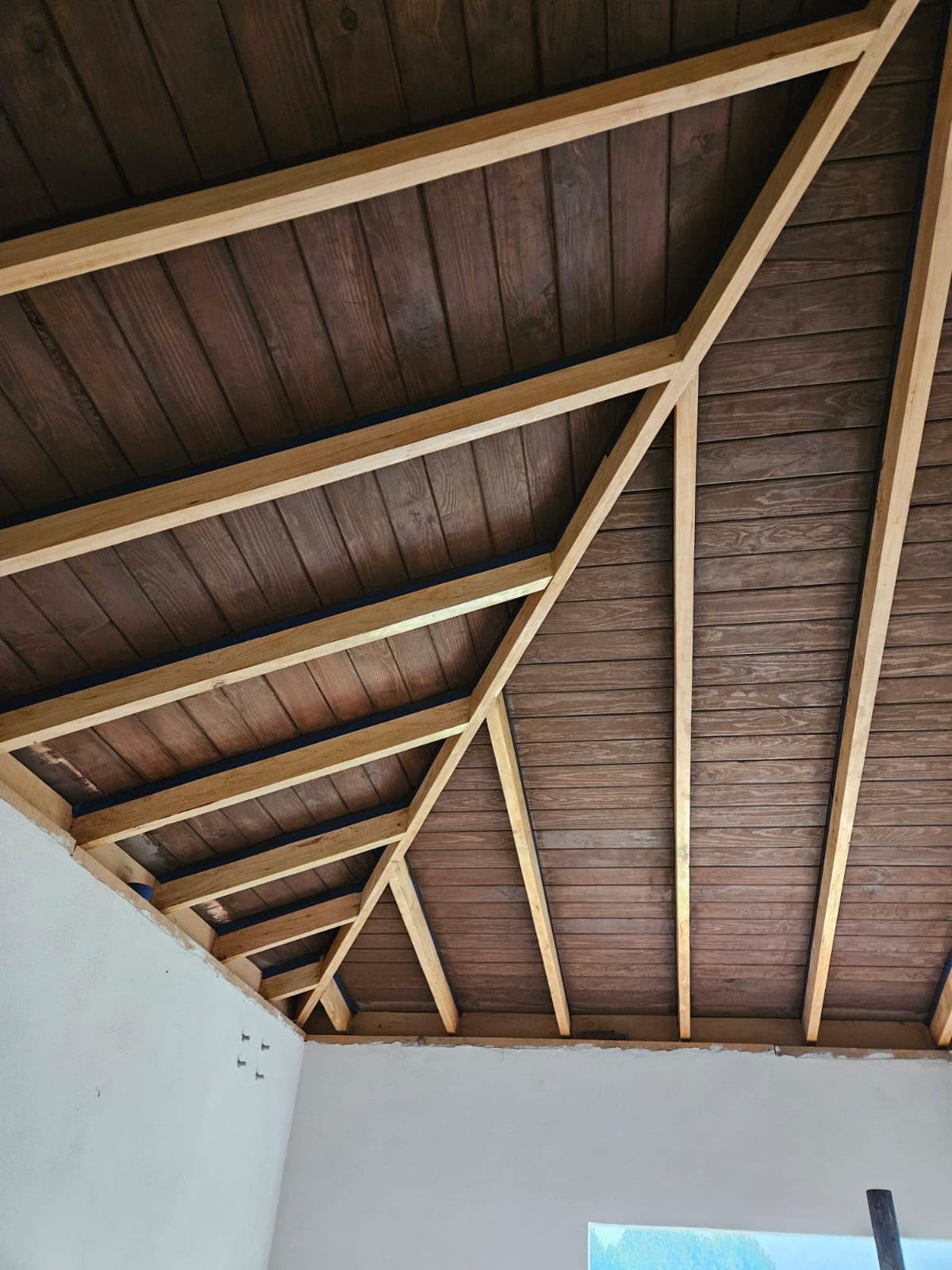 Vista interior de la estructura de madera y el entablado de una cubierta inclinada restaurada.
